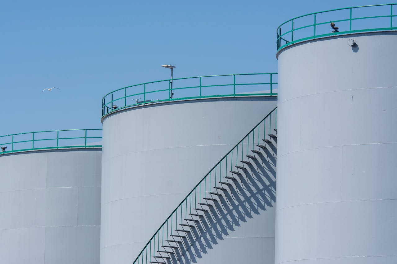 Industrial storage tanks with metal stairways under a clear blue sky, highlighting industrial architecture.